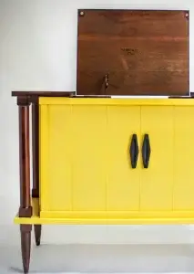Yellow cabinet with wooden top and legs, black handles, and a hinged back panel.