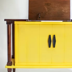 Yellow cabinet with wooden top and legs, black handles, and a hinged back panel.