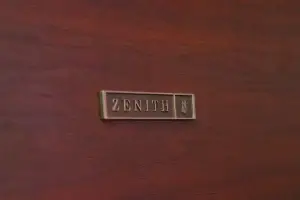 Close-up of the original gold Zenith badge on the finished wood underside of a mid-century stereo console lid.