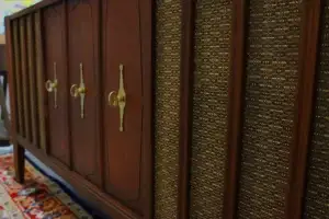 Close-up of gold hourglass-shaped brass pulls and vintage textured speaker grille cloth on a walnut wood Zenith stereo console.