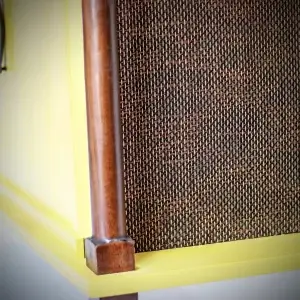 Corner of a yellow cabinet with a wooden trim and woven panel.