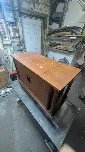 Wooden cabinet on a dolly in a cluttered workshop.