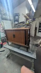 Wooden cabinet on a worktable in a cluttered workshop.