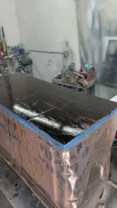 Wooden cabinet with dark stain, wrapped in plastic, on a workbench.
