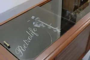 Top-down view of a modern Retrolife turntable visible through the custom-integrated smoked glass top on an RCA Victor console.