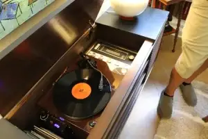 Person standing next to a vintage record player with a vinyl record playing.