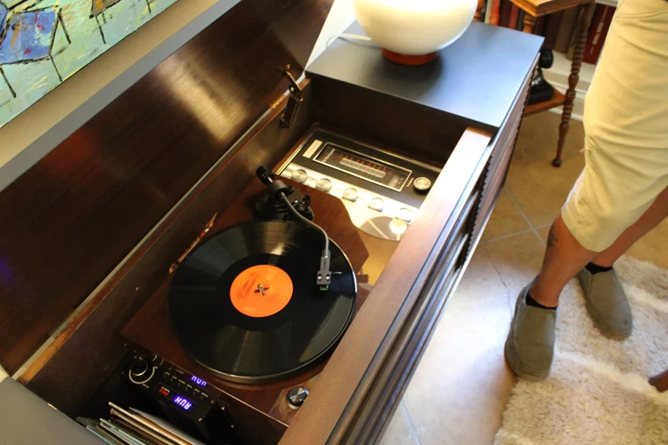 Person standing next to a vintage record player with a vinyl record playing.