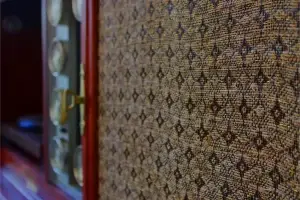 Close-up of the original textured mid-century speaker grille cloth and refinished walnut wood on a Philco stereo console.