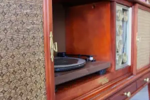 Close-up of polished gold radio knobs and the sliding door pull handle on a refinished Philco mid-century modern stereo console.