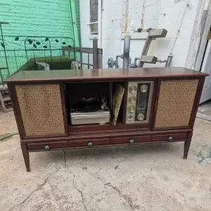A vintage Philco mid-century stereo console in its original, unrestored condition sitting outdoors, showing dusty wood surfaces and the original internal components.