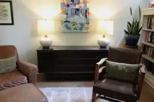 A cozy living room with brown leather chairs, a dark wood Steiner Audio credenza, and a colorful painting on the wall.