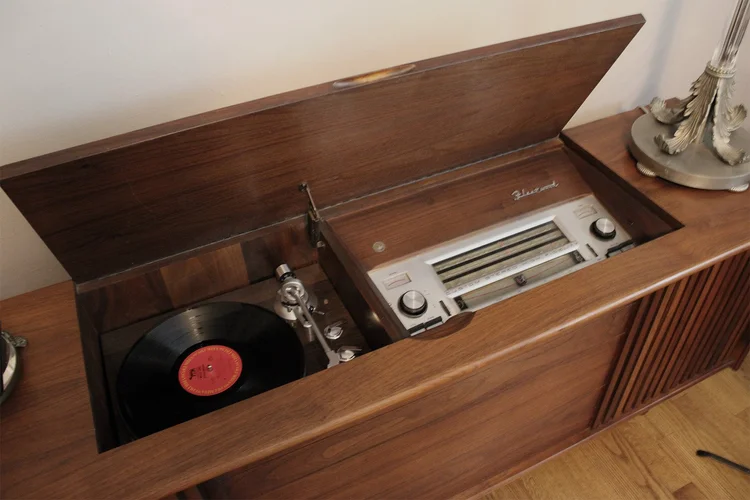 Vintage record player with a vinyl record playing on a wooden cabinet.